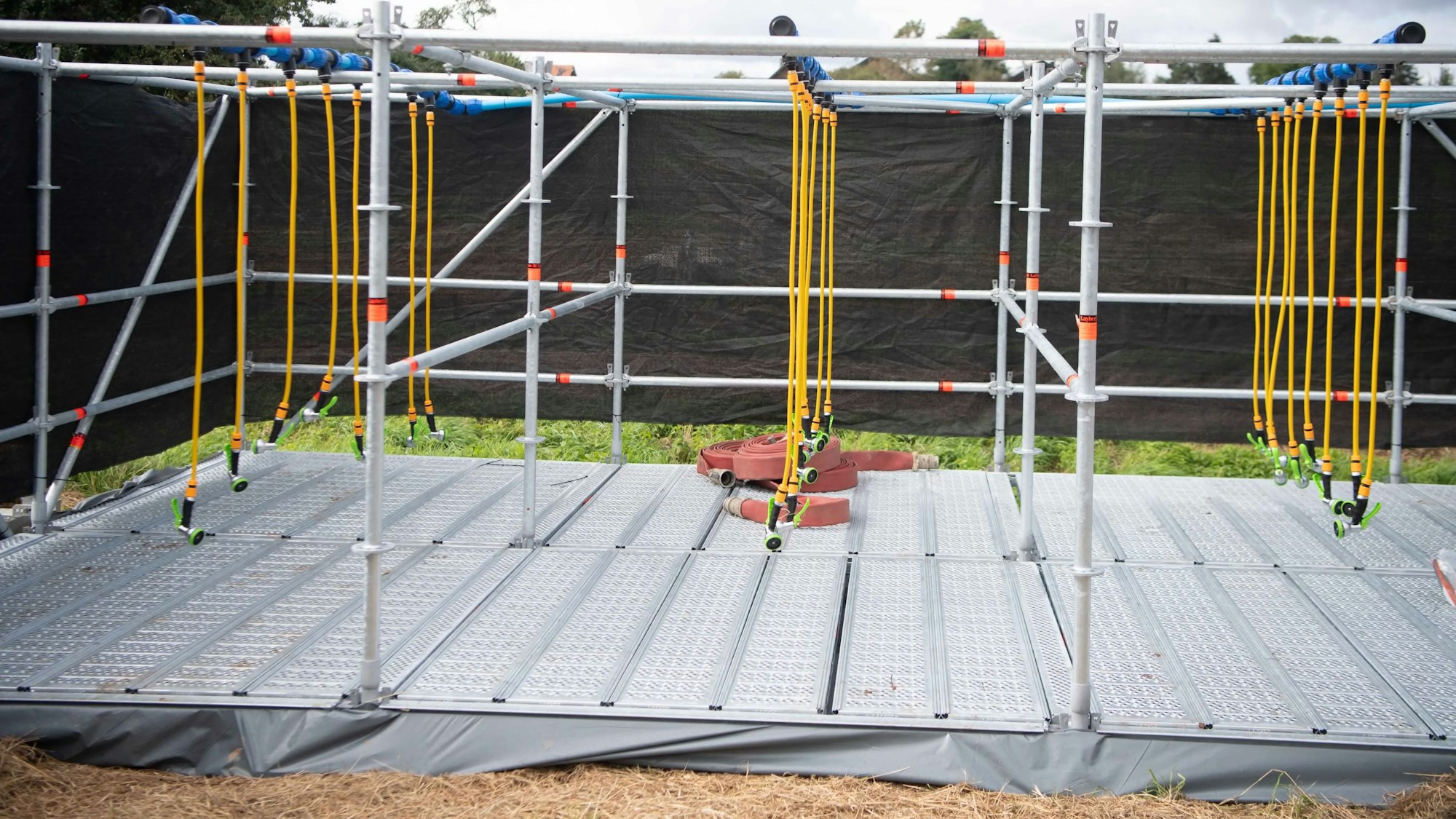 Das Bild zeigt die Dusche beim Tough Mudder. Von einem Stahlgerüst hängen mehrere Schläuche samt Brausen herab.