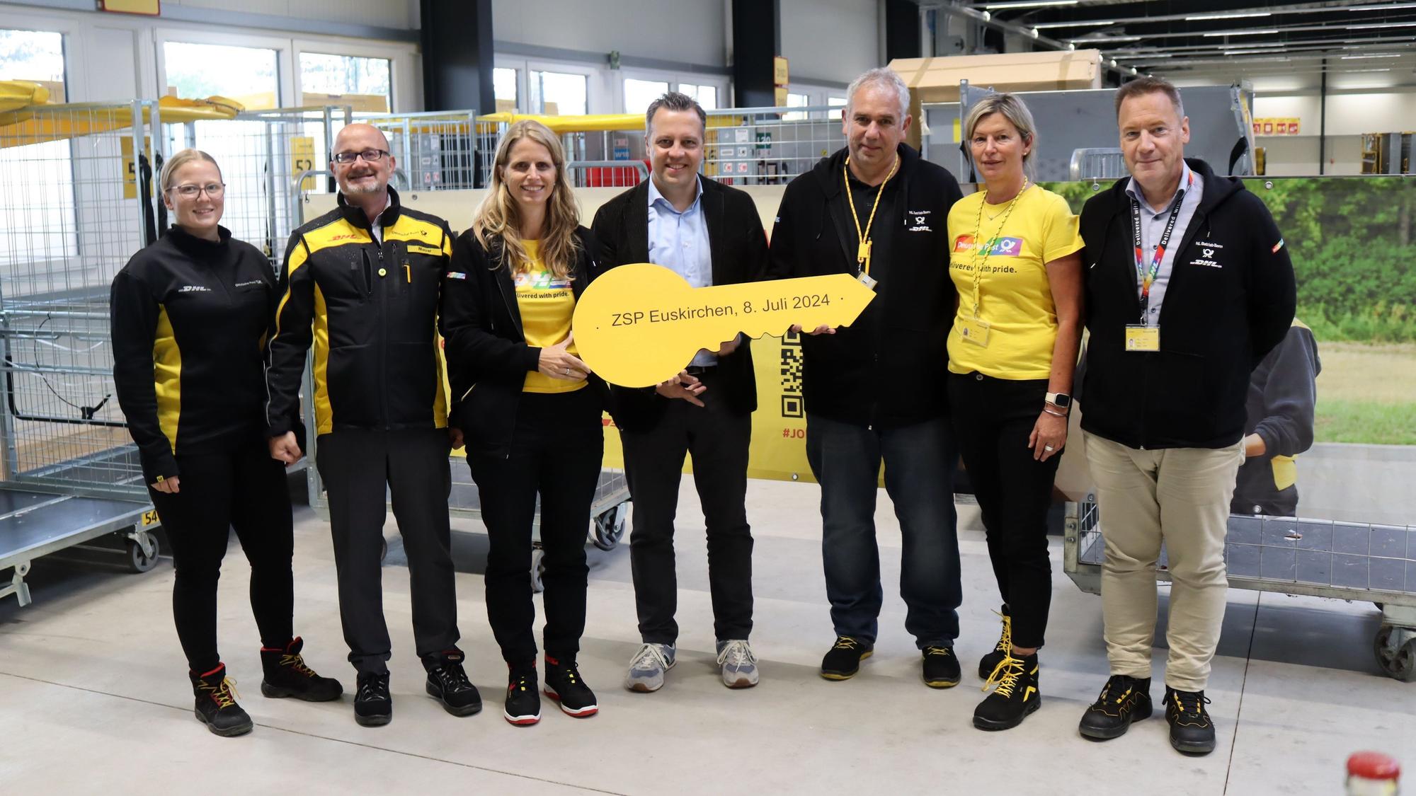 Sechs Mitarbeiter der Post und Euskirchens Bürgermeister posieren für ein Gruppenfoto. Der Bürgermeister hält einen riesigen gelben Schlüssel in den Händen.