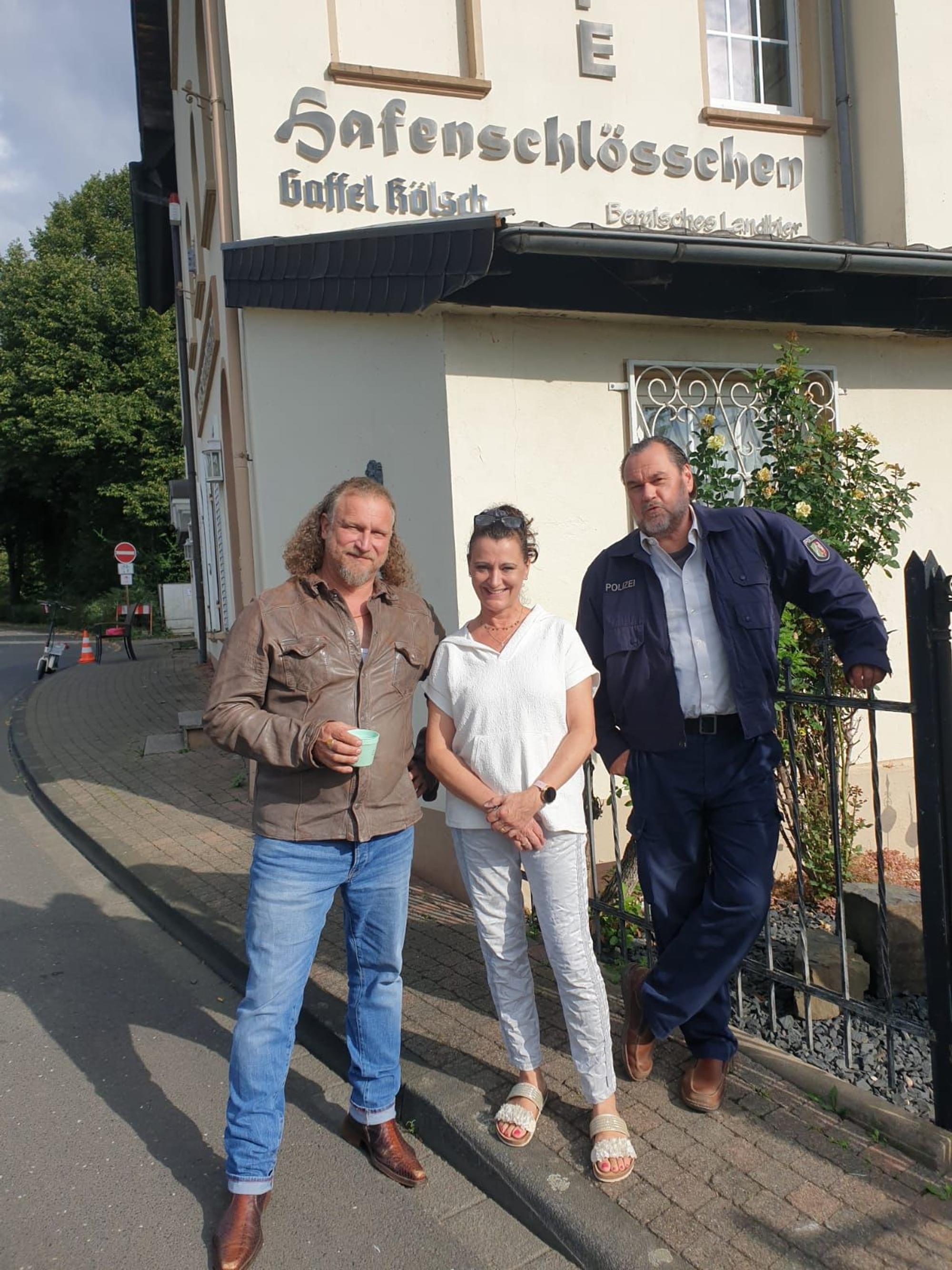 Zwei Männer und eine Frau stehen vor einem Gebäude.