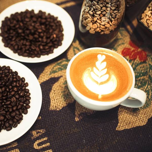 Ein Cappuccino mit einem Muster aus Herzen neben frischen Kaffeebohnen.