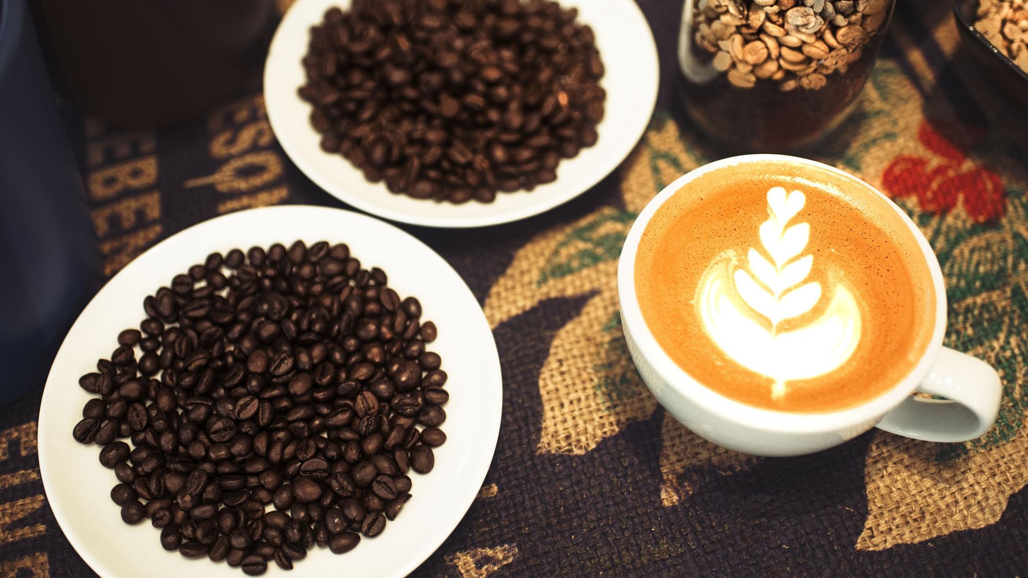 Ein Cappuccino mit einem Muster aus Herzen neben frischen Kaffeebohnen.