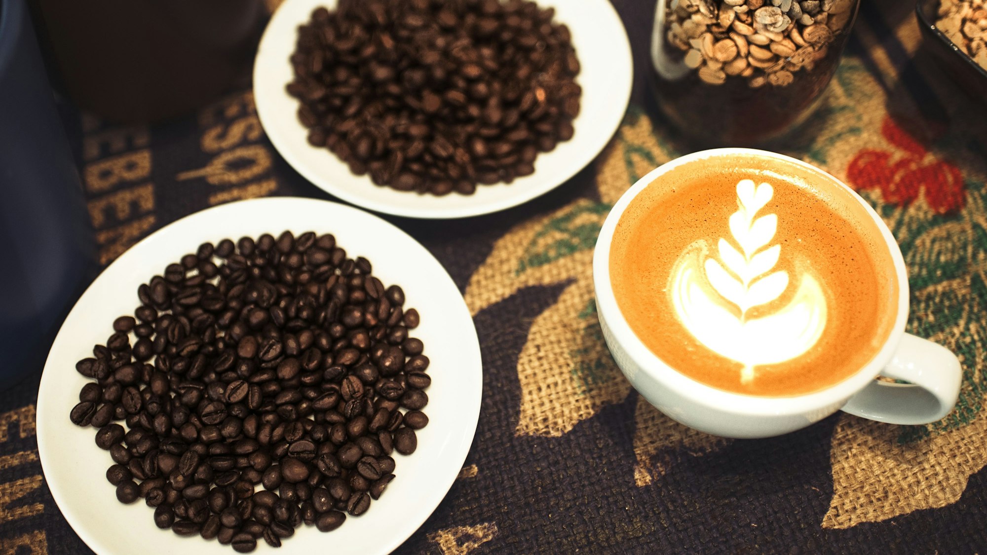Ein Cappuccino mit einem Muster aus Herzen neben frischen Kaffeebohnen.
