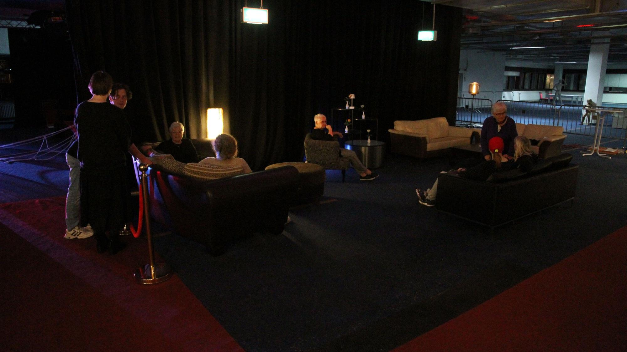 Menschen sitzen vor einem Theater in Polstermöbeln