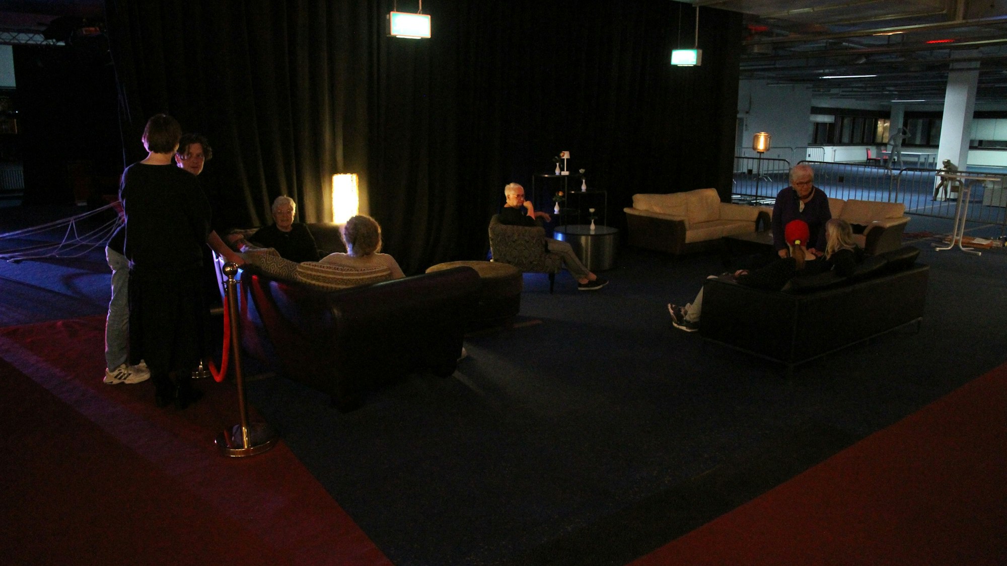 Menschen sitzen vor einem Theater in Polstermöbeln