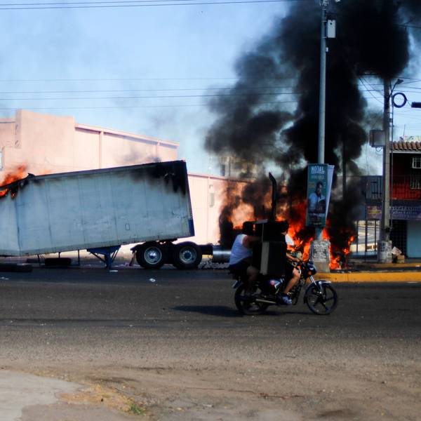 Männer fahren am 4. Januar 2023 auf einem Motorrad an einem brennenden Lastwagen in den Straßen von Culiacán im Bundesstaat Sinaloa vorbei.