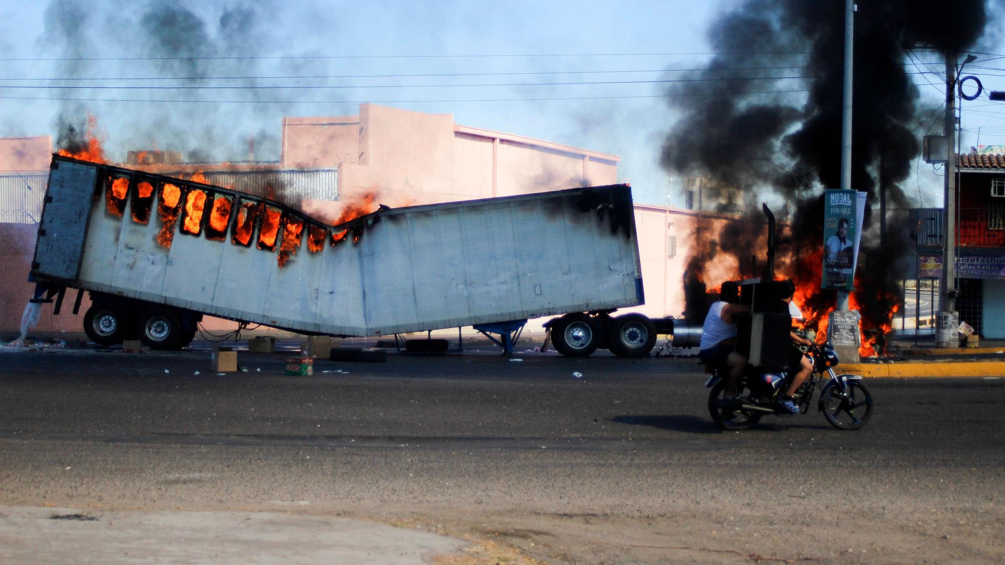 Männer fahren am 4. Januar 2023 auf einem Motorrad an einem brennenden Lastwagen in den Straßen von Culiacán im Bundesstaat Sinaloa vorbei.