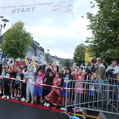 Ein Tiermaskottchen winkt einer großen Kindergruppe.