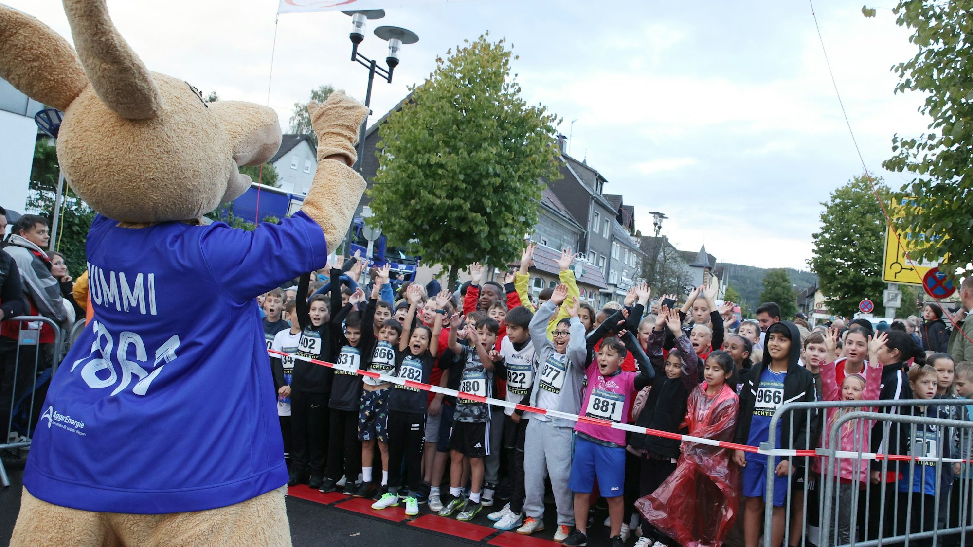 Ein Tiermaskottchen winkt einer großen Kindergruppe.