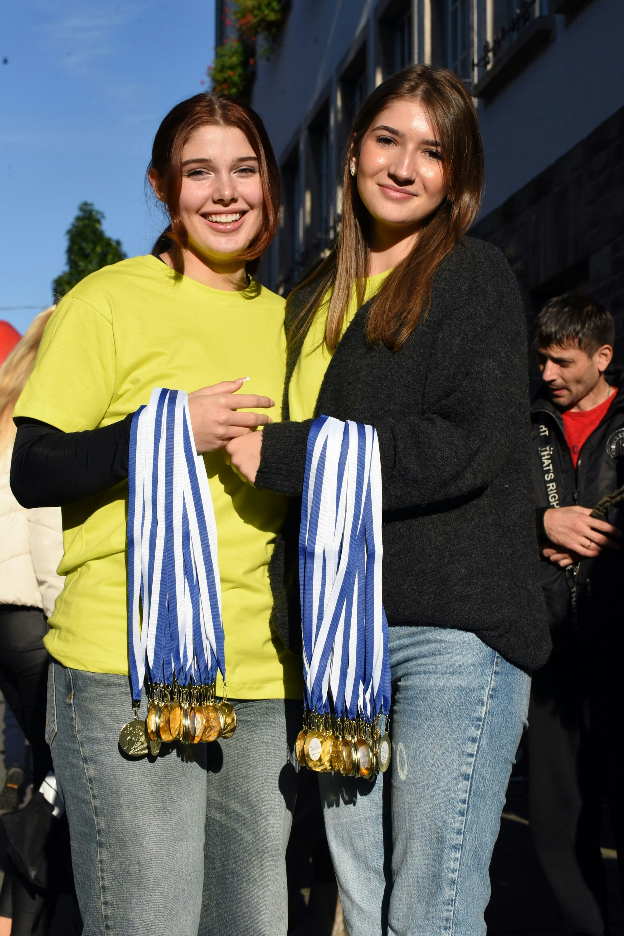 Zu sehen sind zwei junge Frauen, die jeweils viele Medaillen an ihrem Arm tragen.