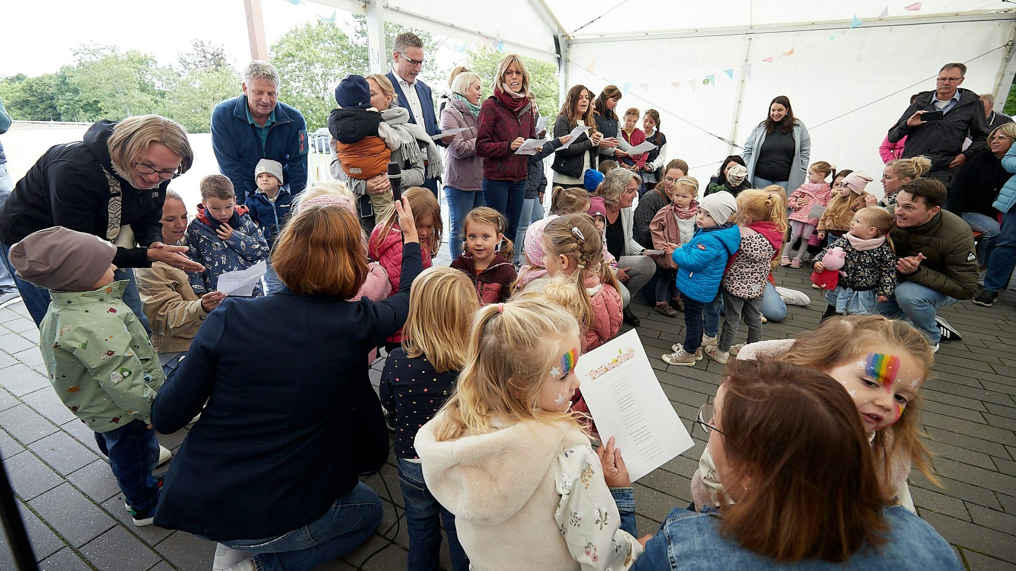Zahlreiche Kinder stehen in Nettersheim in einem Zelt und singen zur Eröffnung ihrer Kita ein Lied.
