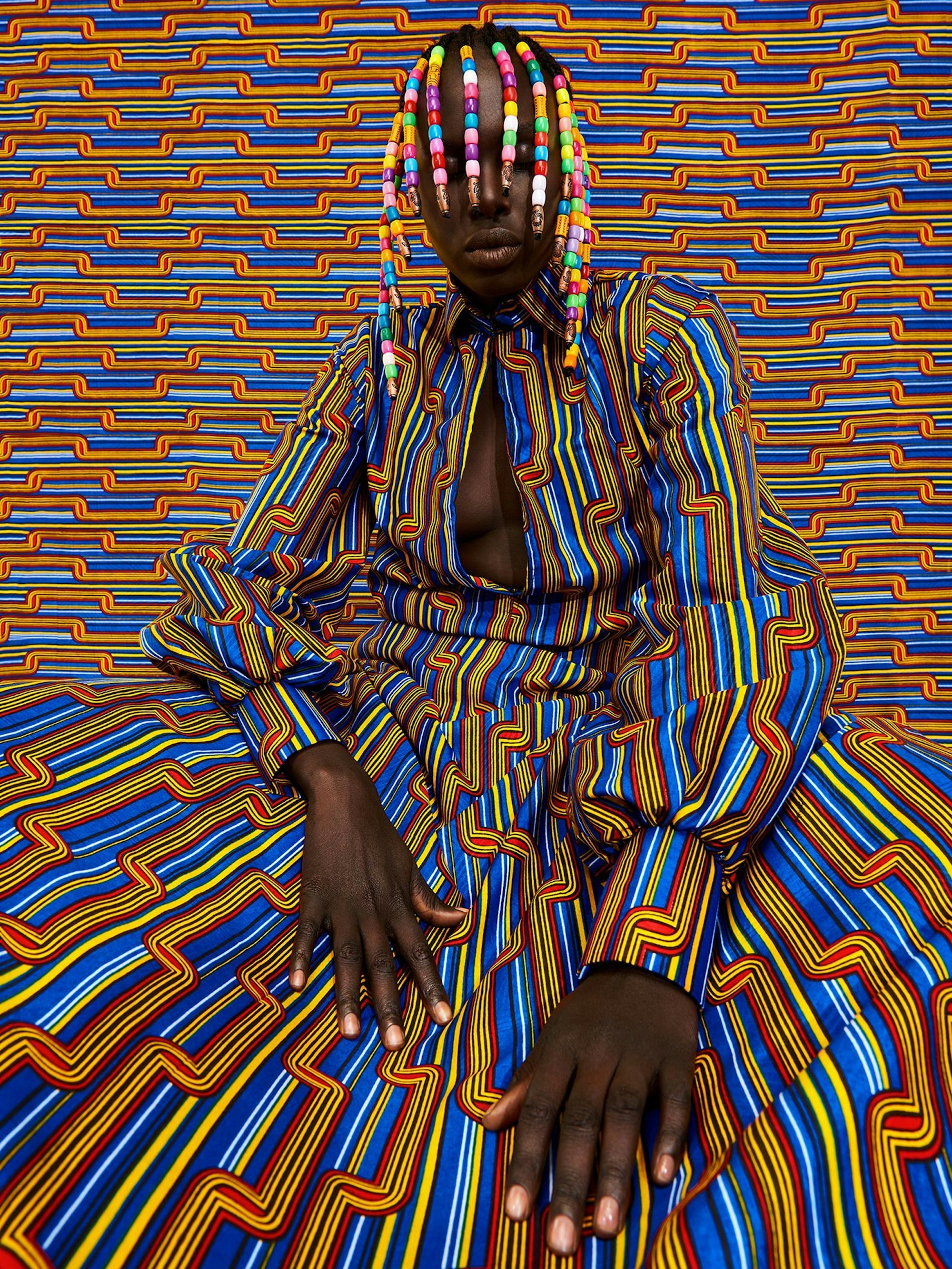 Eine Frau trägt ein buntes Kleid und bunte Erweiterungen im Haar.