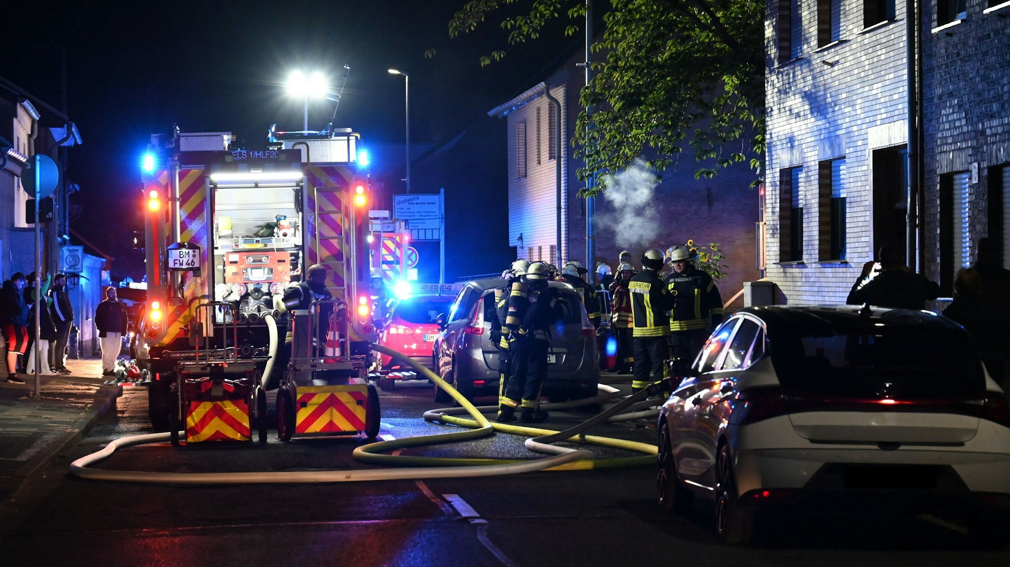 Ein Feuerwehrfahrzeug und eine Gruppe Feuerwehrleute steht in der Dunkelheit vor einem Haus.