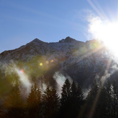 Morgennebel steigt über den Wiesen vor den Gipfeln des schneebedeckten Karwendelgebirges auf.