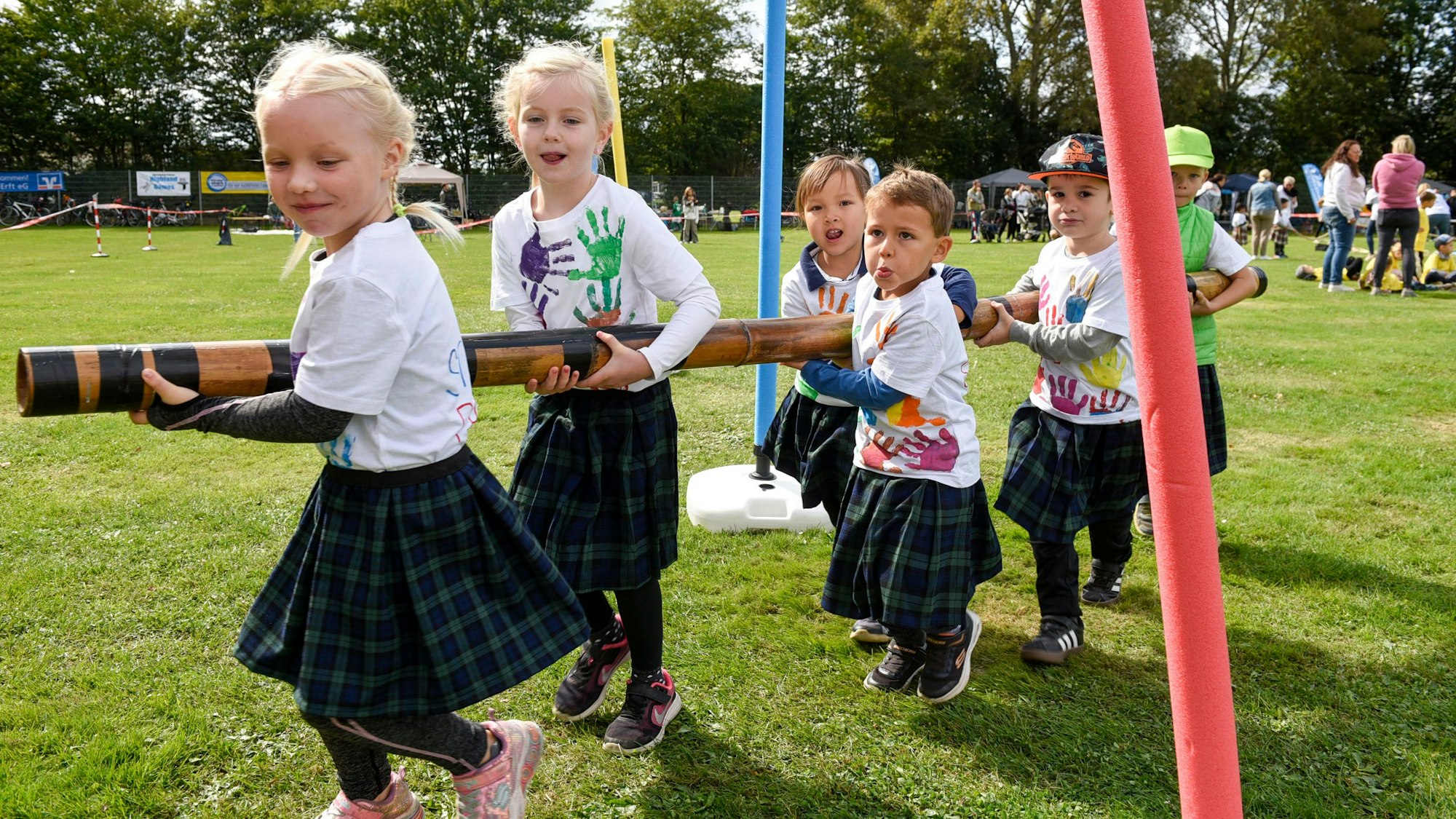 Eine Bambusstange tragen die Kinder durch den Slalomparcours.