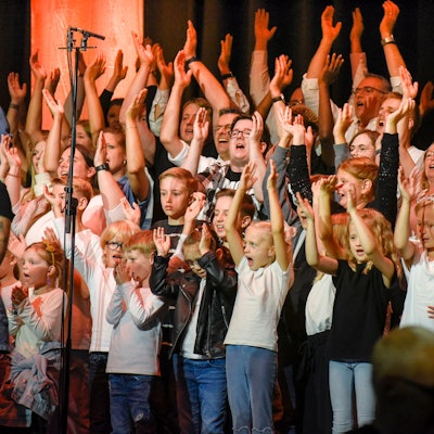 Zahlreiche Kinder und Erwachsene werfen die Arme in die Luft.