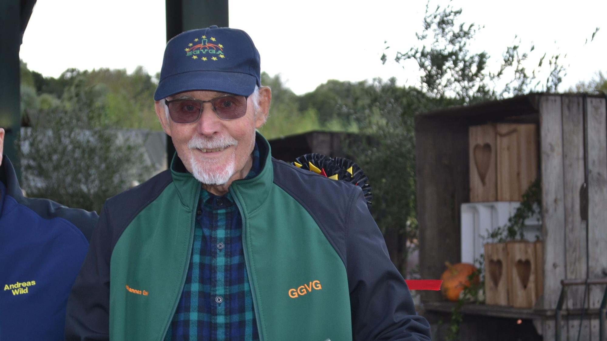 Ein älterer Mann in grüner Jacke und mit Käppi.