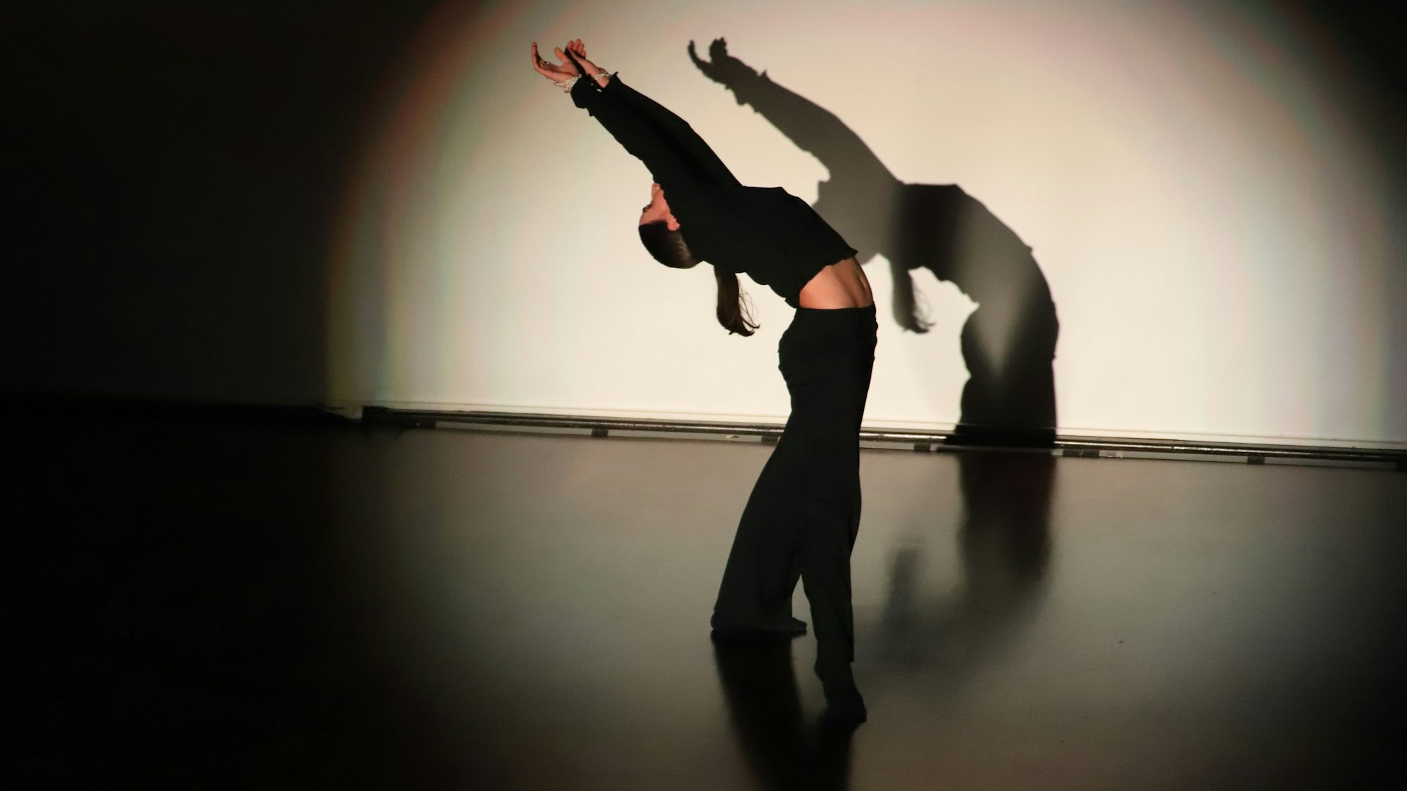 Eine Tänzerin bewegt sich und wirft Schatten im Scheinwerferlicht.