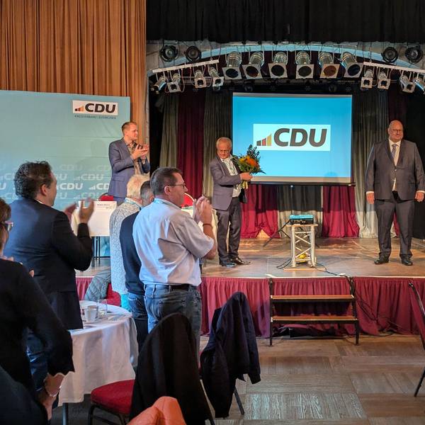 Männer applaudieren einem anderen Mann auf einer Bühne mit einem CDU-Plakat.