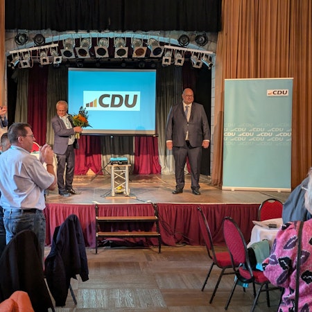 Männer applaudieren einem anderen Mann auf einer Bühne mit einem CDU-Plakat.