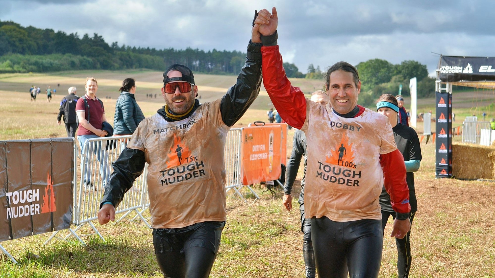 Die beiden Männer recken triumphierend ihre zusammengebundenen Hände in die Luft. Im Hintergrund steht Publikum.