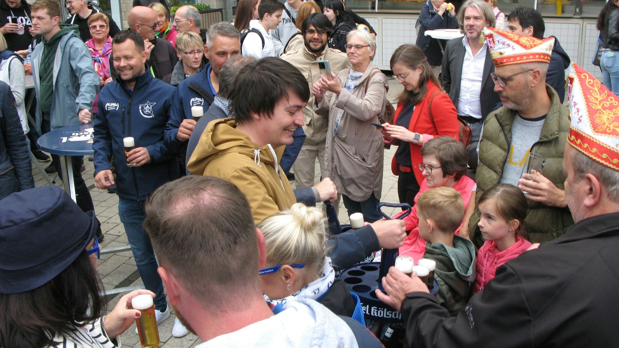 Der Bürgermeister Mario Dahm steht mit einem Gläserkranz in einer Menschenmenge und bietet Bier an.