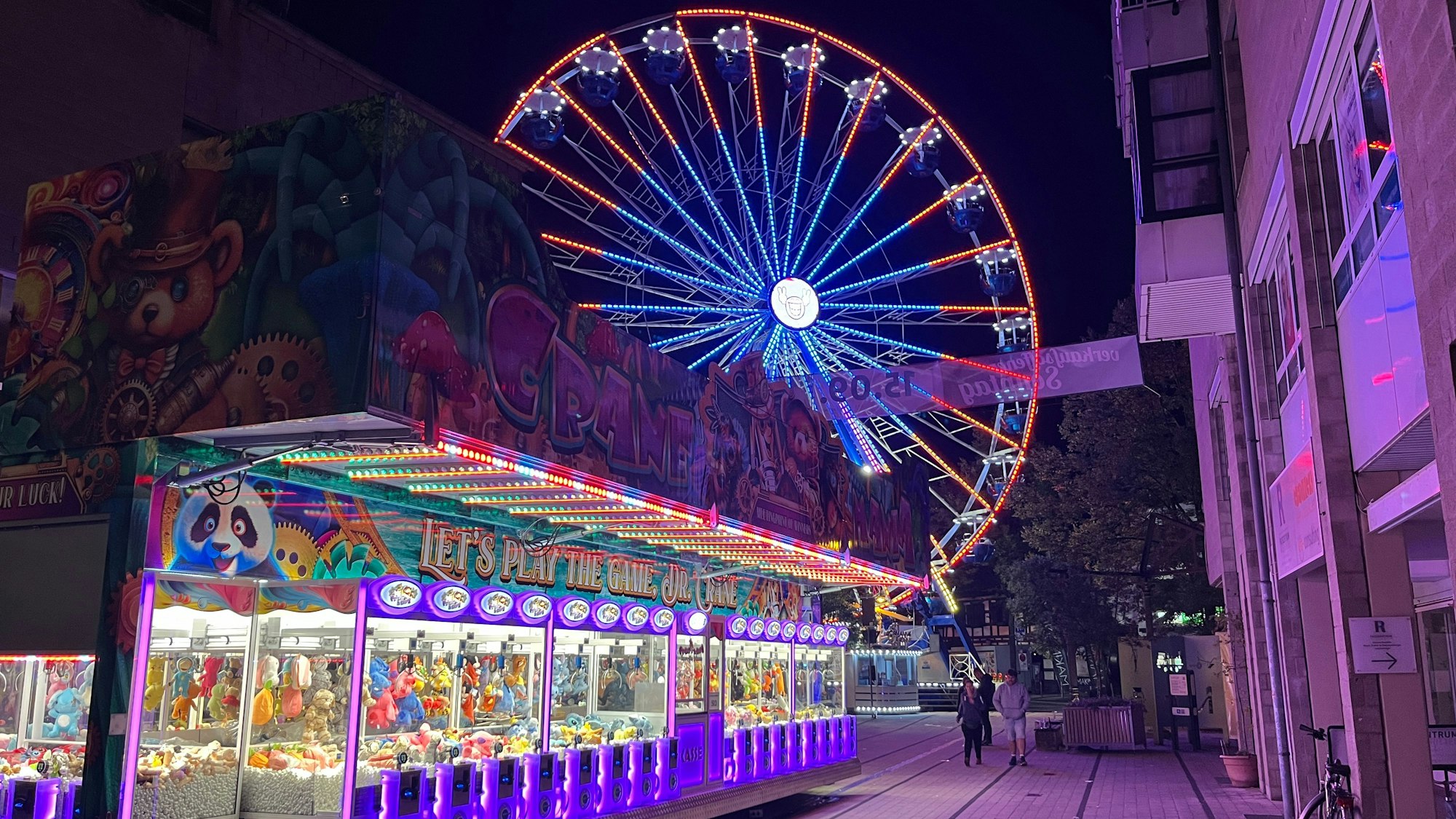 Ein Riesenrad dreht sich hinter einer Glücksspielbude.