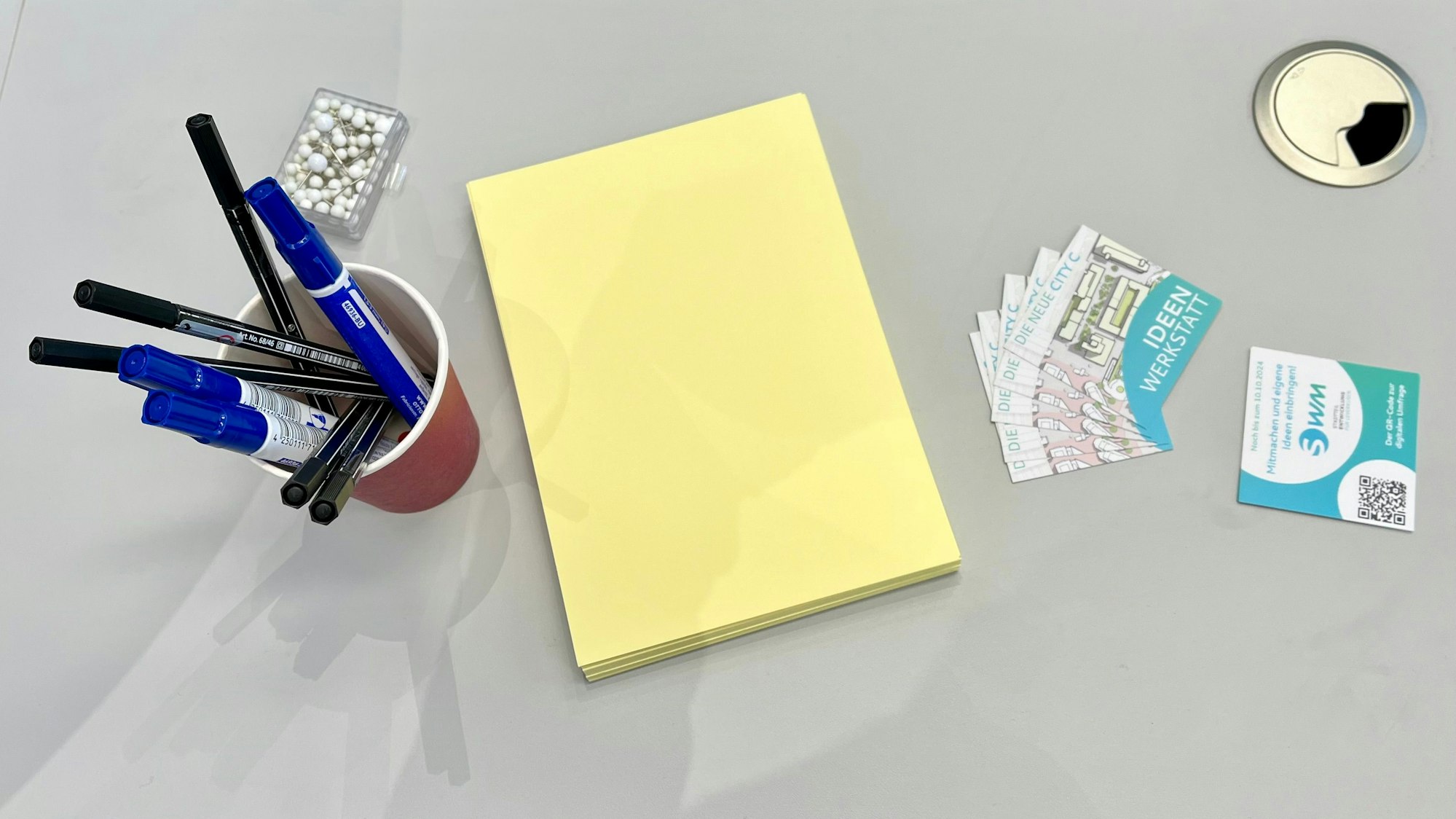 Stifte, Notizzettel und Kärtchen mit einem QR-Code auf einem Tisch.