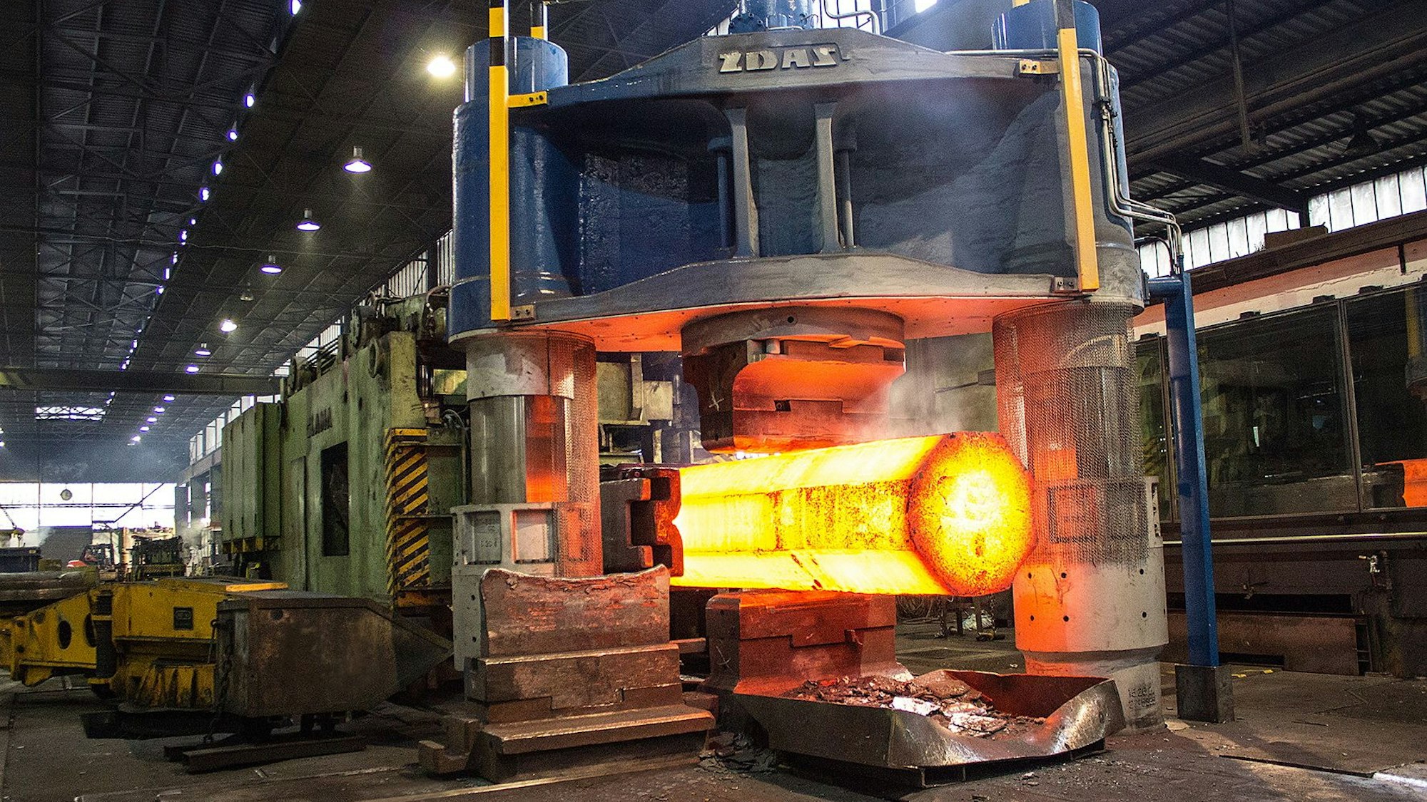 Ein glühender Block Stahl kommt aus einer Presse.