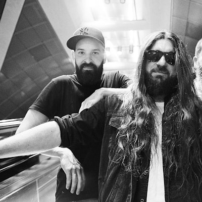 Auf der Schwarz-Weiß-Fotografie stehen drei Musiker auf einer U-Bahn-Rolltreppe.
