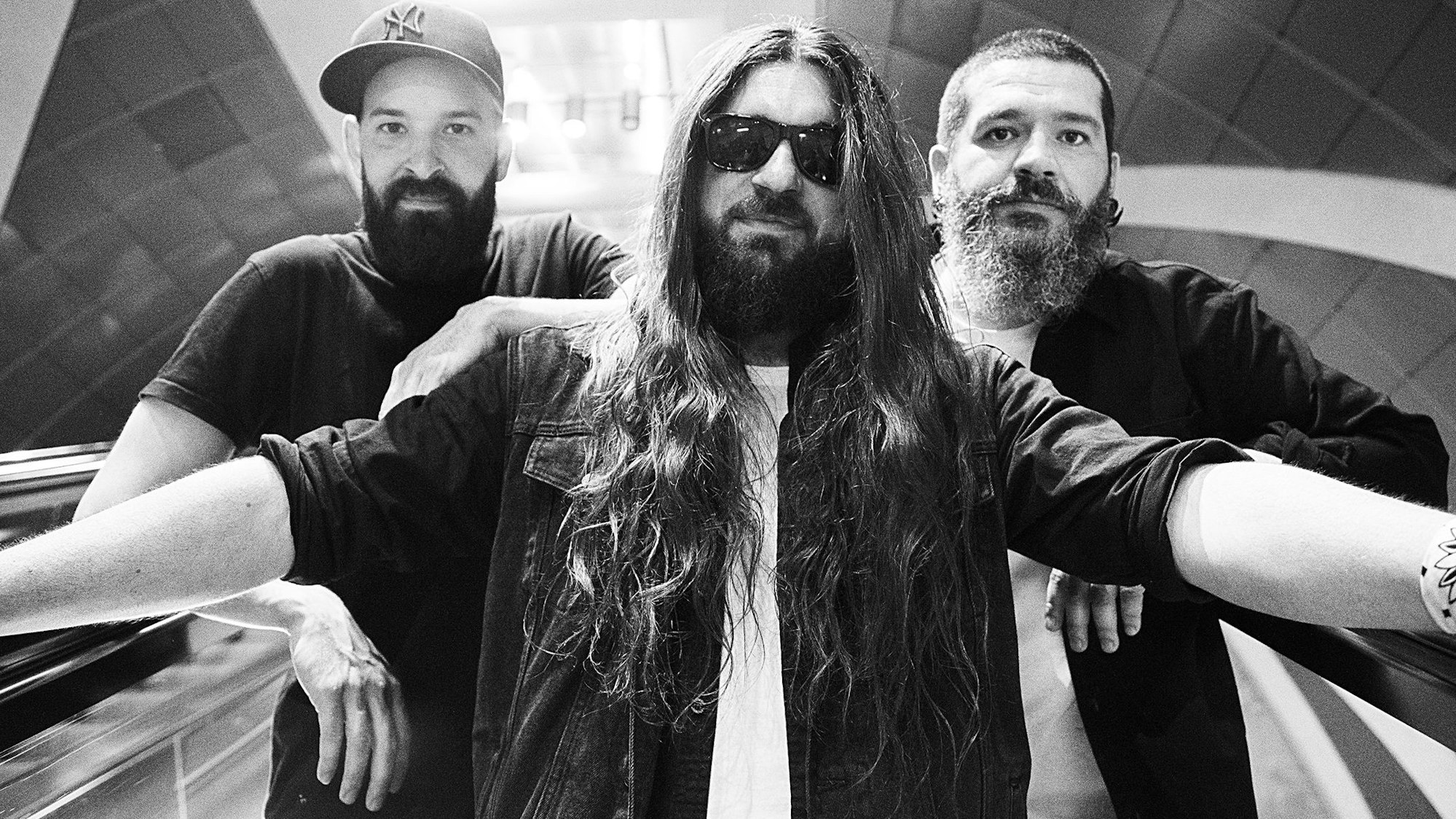 Auf der Schwarz-Weiß-Fotografie stehen drei Musiker auf einer U-Bahn-Rolltreppe.