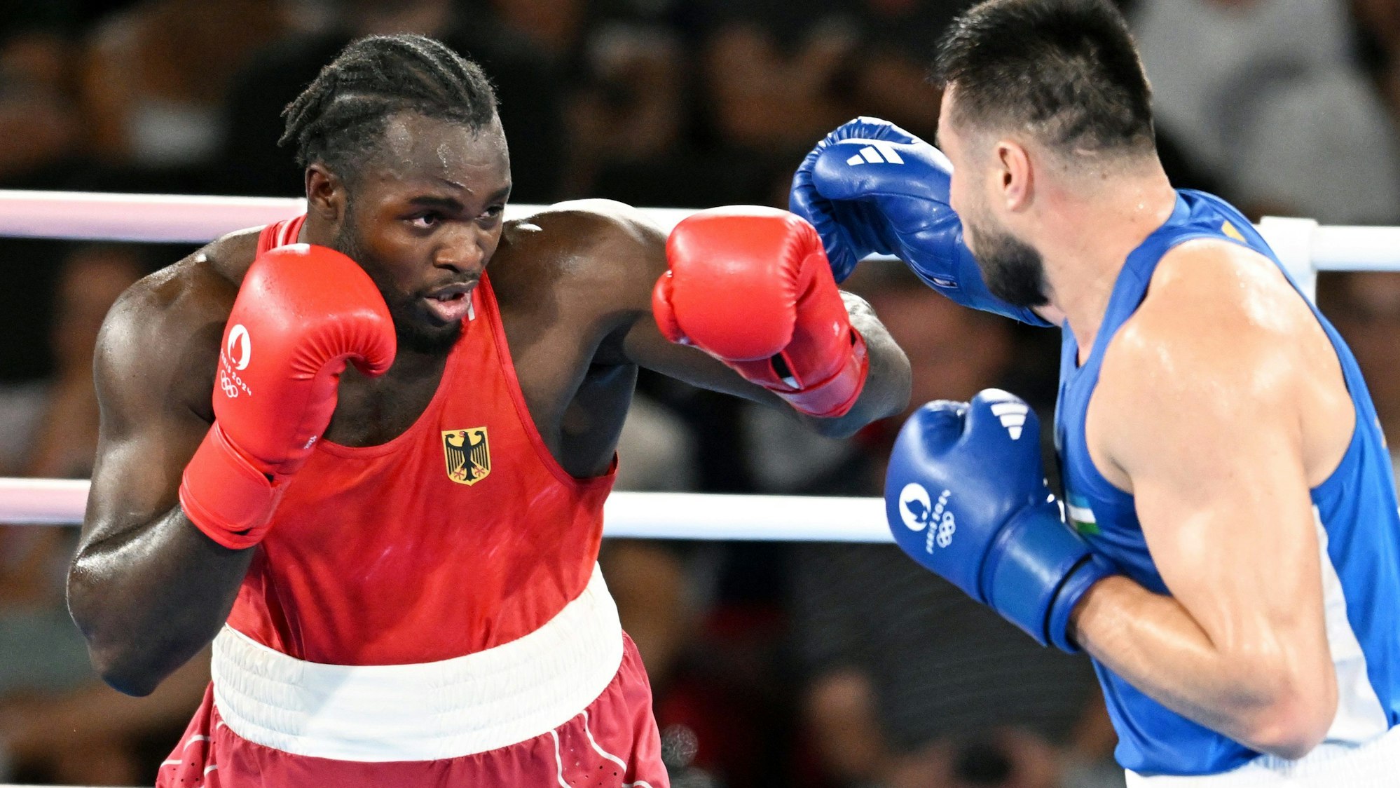 Boxer Nelvie Tiafack kämpft im roten Trikot im Halbfinale bei den Olympischen Spielen in Paris gegen Bakhodir Jalolov im blauen Trikot.