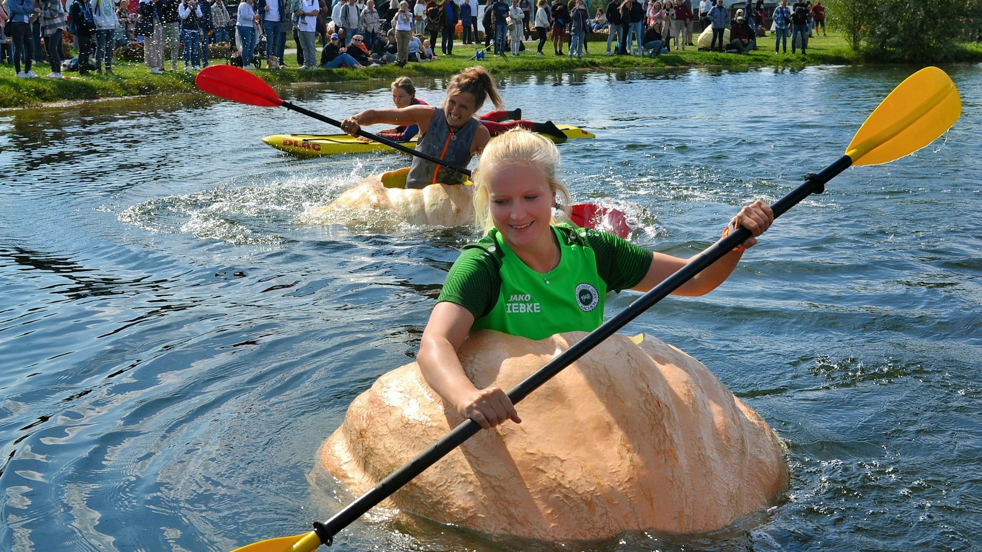 Die jungen Frauen paddeln in ihren Kürbisbooten über den See.