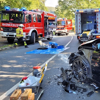 Ein Auto mit Totalschaden steht vor Feuerwehrfahrzeugen.