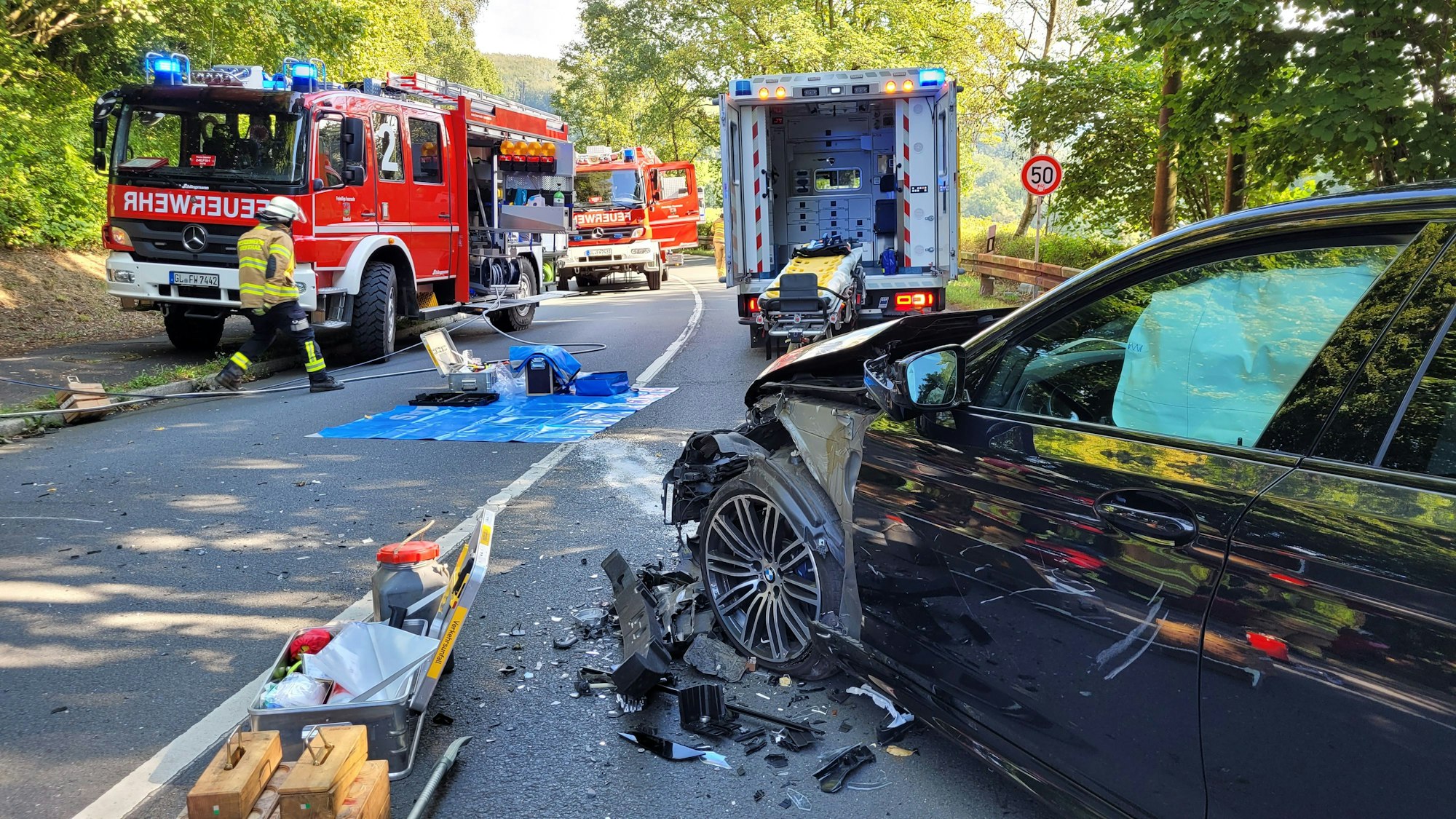 Ein Auto mit Totalschaden steht vor Feuerwehrfahrzeugen.