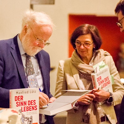 Manfred Lütz ist links im Bild, er signiert ein Buch. Neben ihm stehen eine Frau und ein Mann.