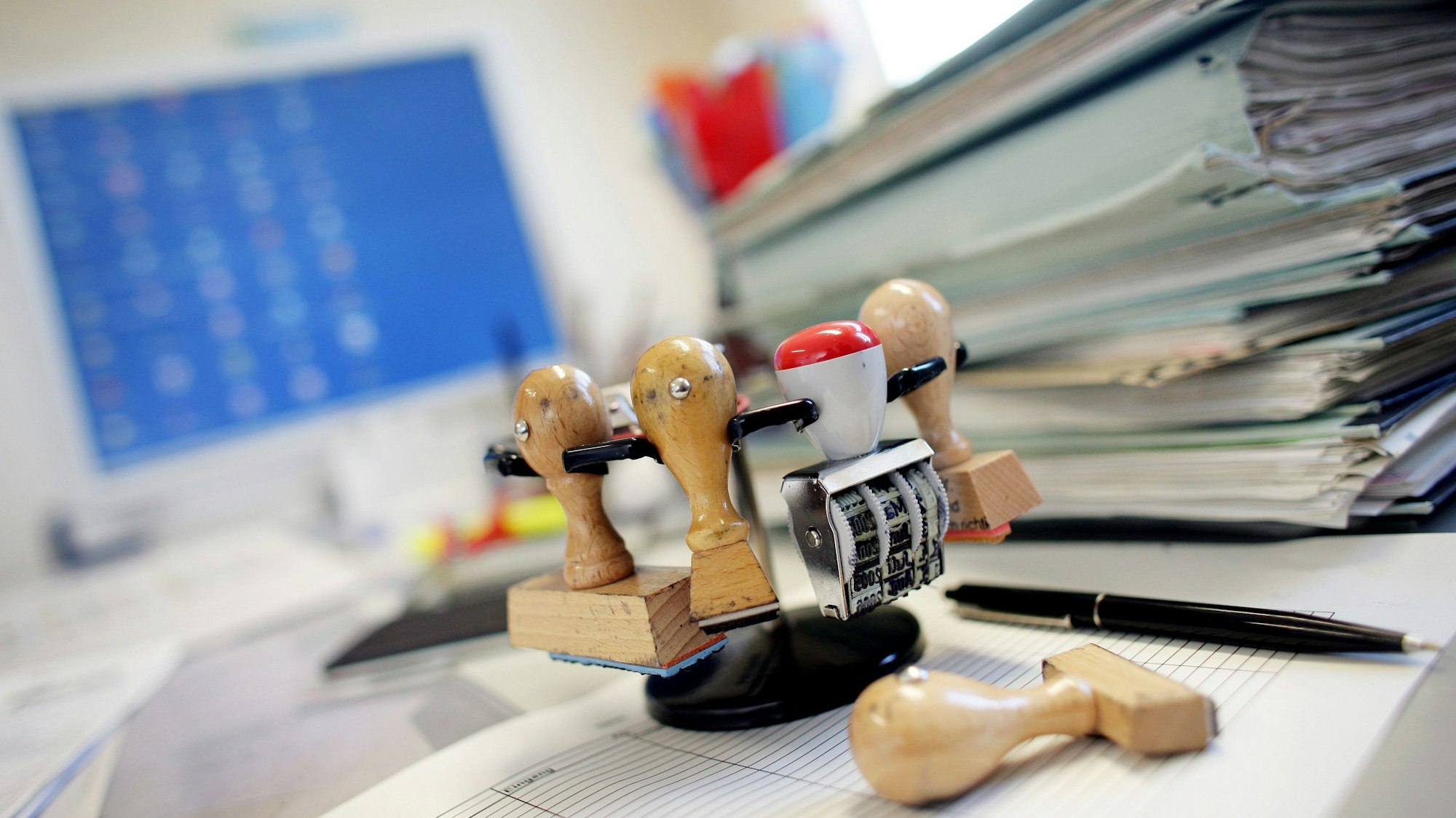 Ein Stempelkarussell steht neben einem Stapel Akten auf einem Schreibtisch in einer Behörde.