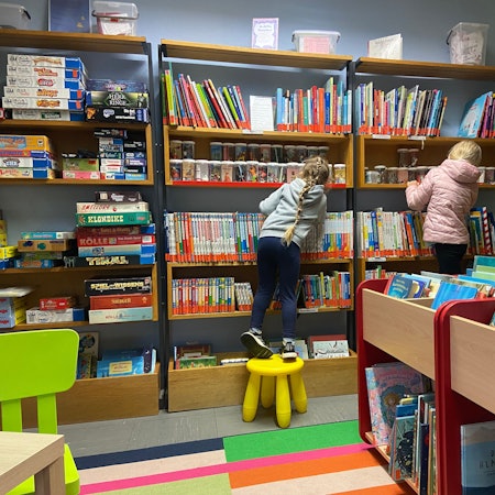 Zu sehen sind zwei Kinder, die vor einem großen Bücherregal stehen.