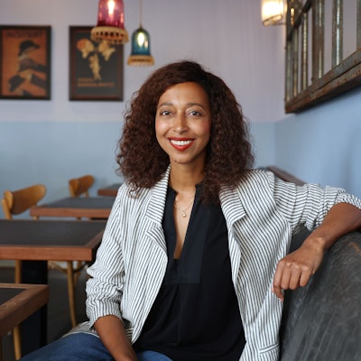 Melanie Raabe sitzt in einem Kölner Café. Sie trägt ein schwarzes Oberteil und einen gestreiften hellen Blazer.