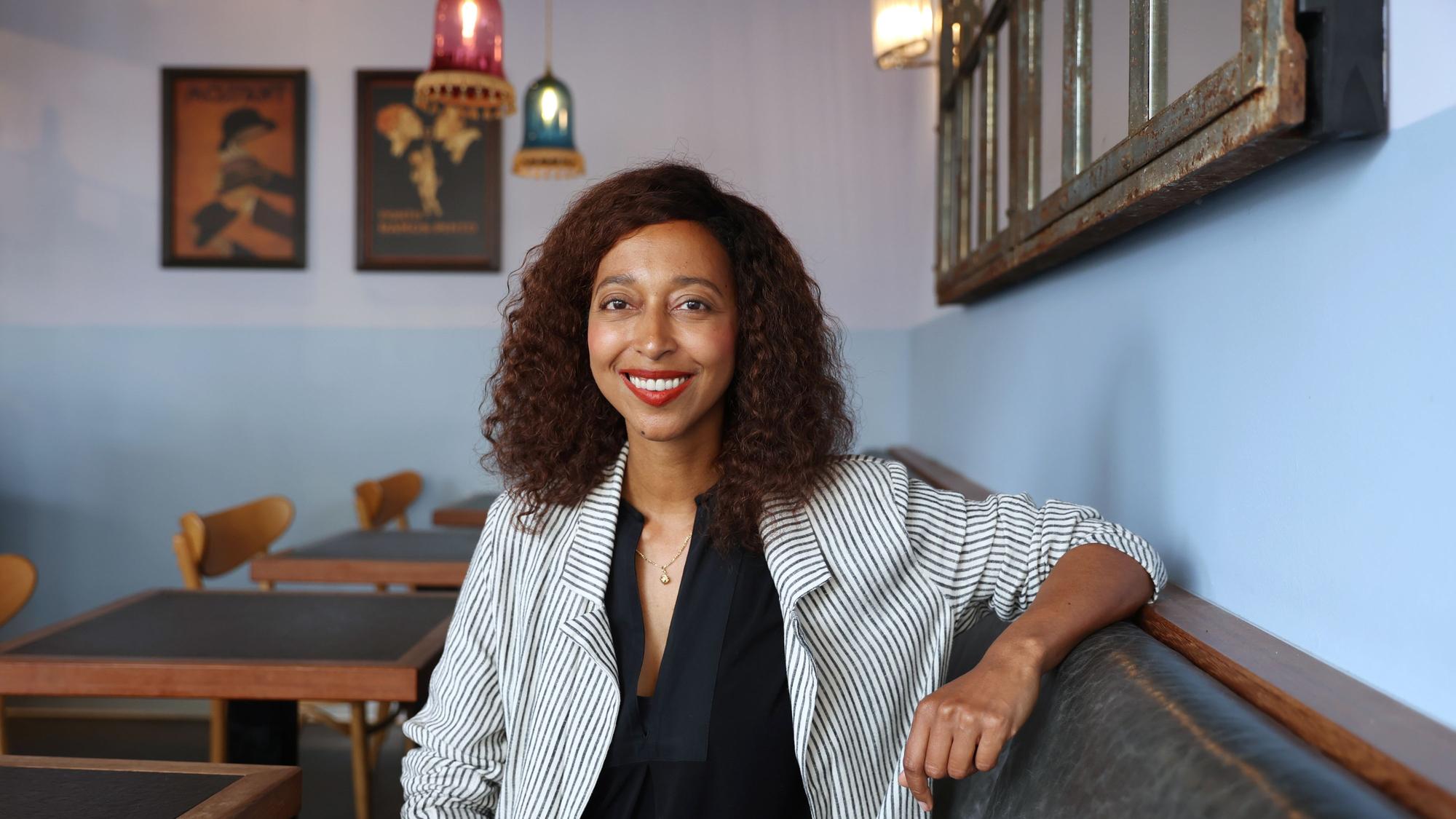 Melanie Raabe sitzt in einem Kölner Café. Sie trägt ein schwarzes Oberteil und einen gestreiften hellen Blazer.