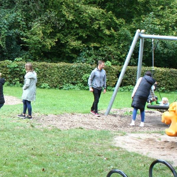Ein Spielplatz mit Kindern, Erwachsenen, Schaukeln und Klettergerüsten.
