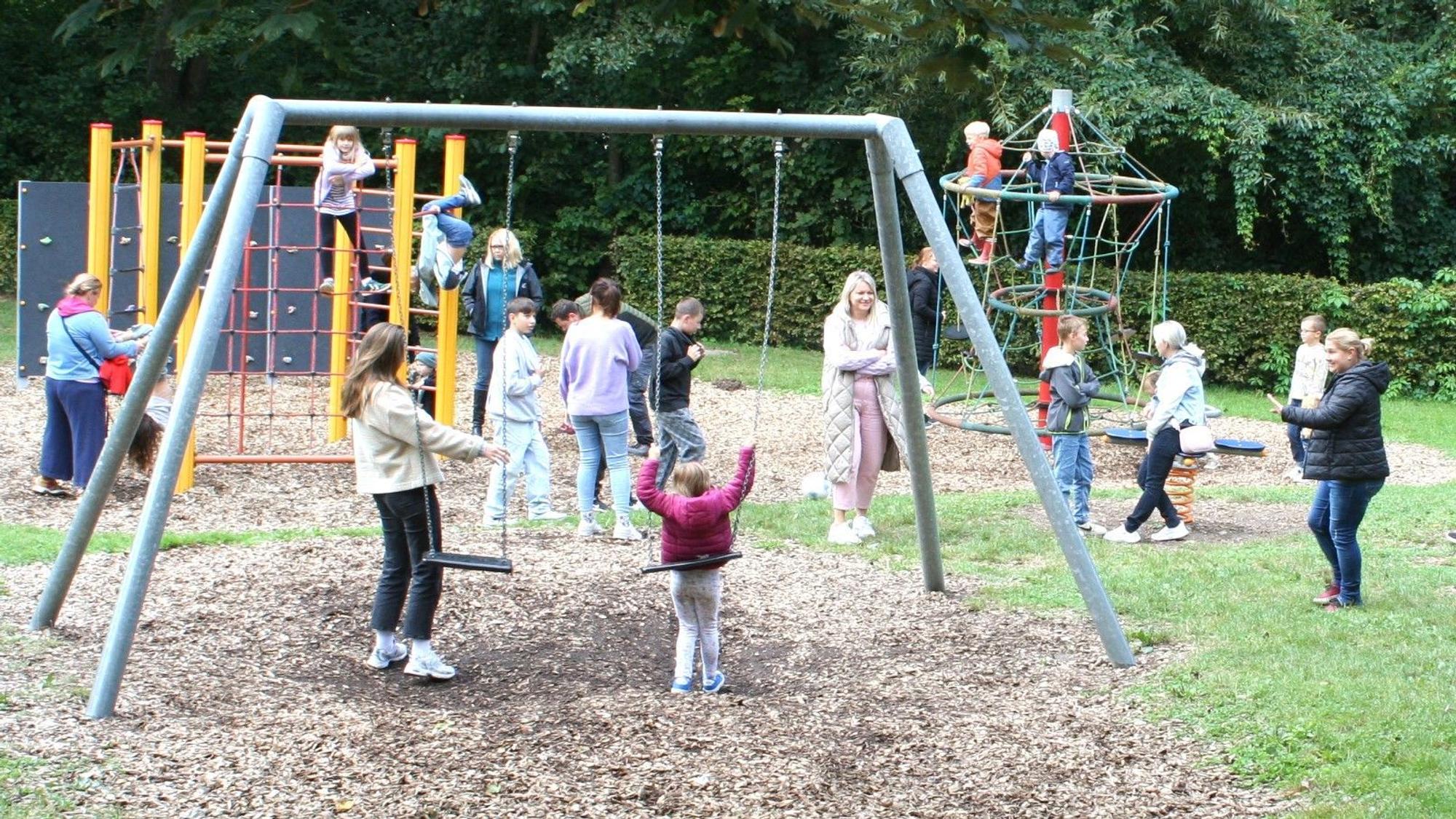 Ein Spielplatz mit Kindern, Erwachsenen, Schaukeln und Klettergerüsten.