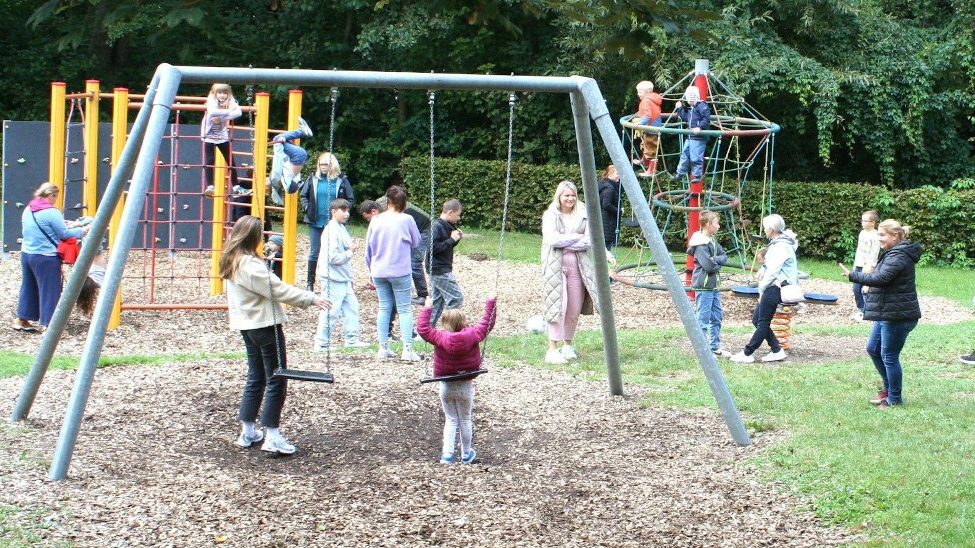 Ein Spielplatz mit Kindern, Erwachsenen, Schaukeln und Klettergerüsten.