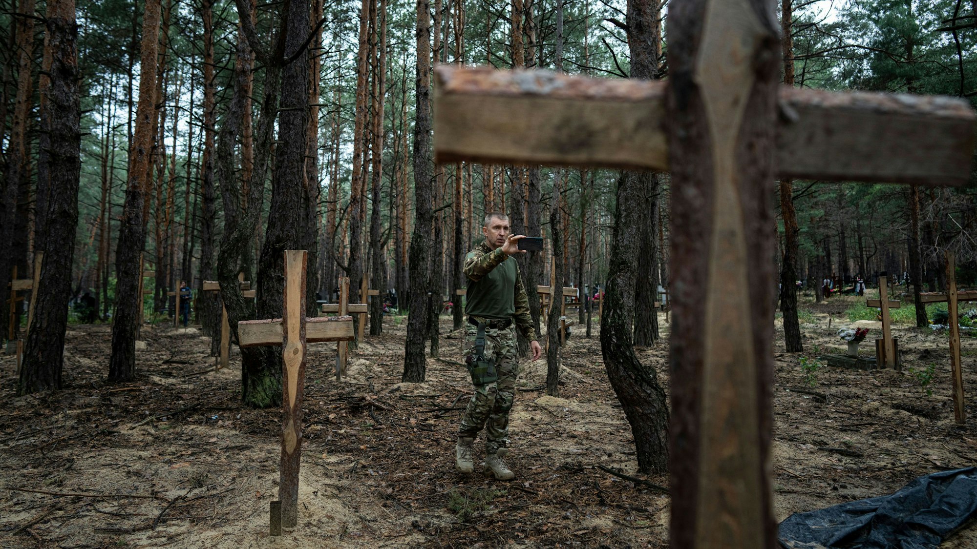 Ein Ukrainer filmt die nicht identifizierten Gräber von Zivilisten und ukrainischen Soldaten, die von den russischen Streitkräften zu Beginn des Krieges im Gebiet Izium getötet worden waren. (Archivbild)