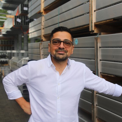 Ein Mann mit Brille steht vor Aluminiumprofilen.