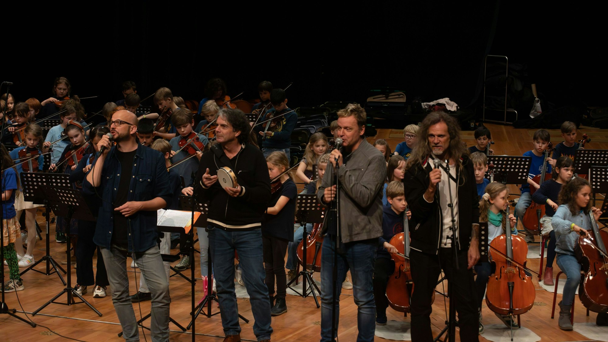 Mitglieder der Bläck Fööss spielen gemeinsam mit Kindern  bei einem Auftritt in der Musikhochschule anlässlich des Jubiläums „20 Jahre Klassenstreicher“ der Helmut-Behn-Stiftung.