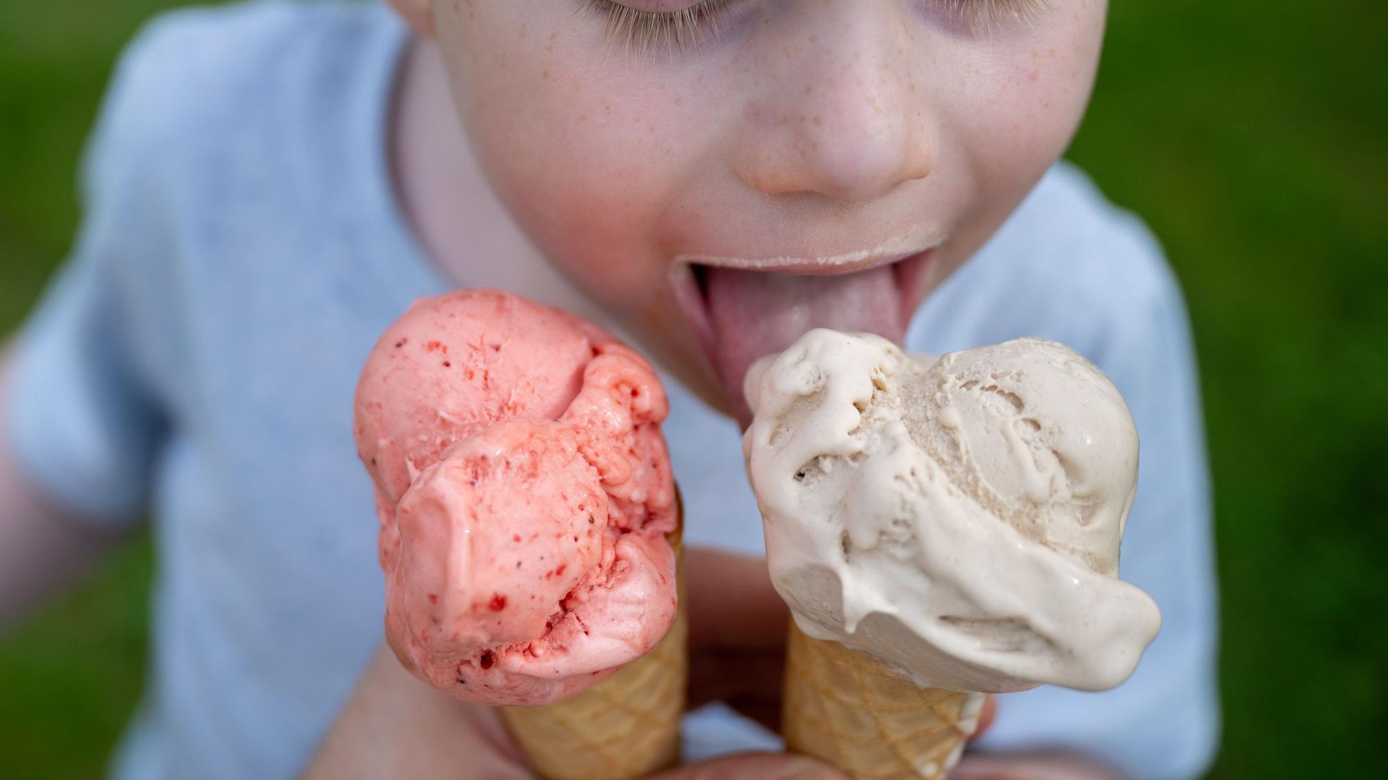 Ein Kleinkind leckt bei sommerlichen Temperaturen an einem Eis in der Waffel.