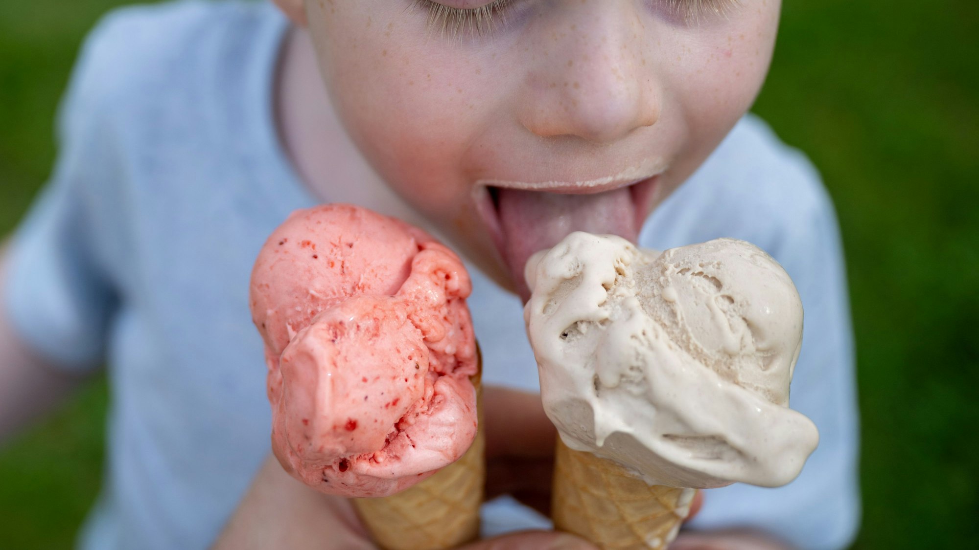 Ein Kleinkind leckt bei sommerlichen Temperaturen an einem Eis in der Waffel.