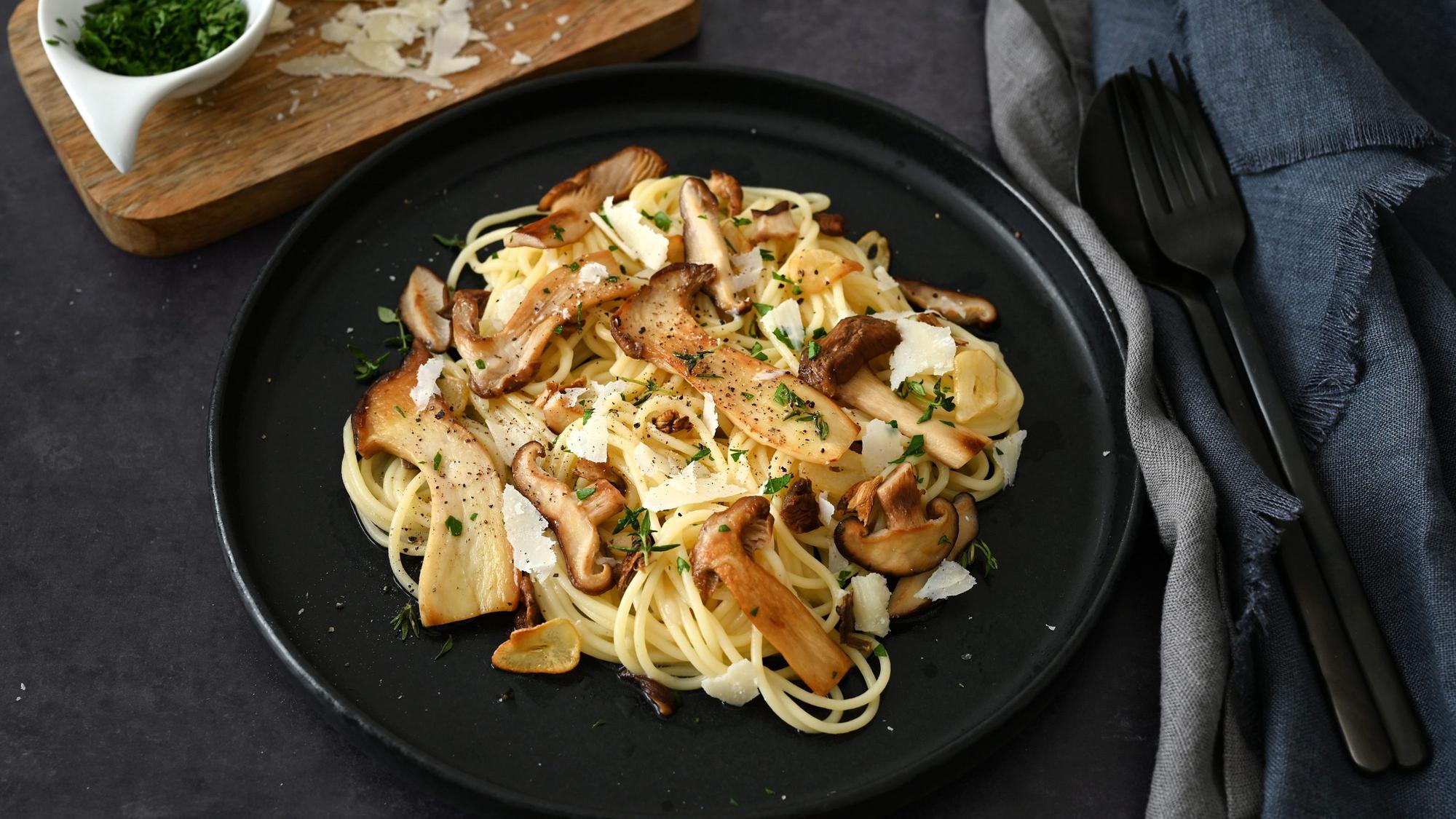 Spaghettini liegen auf einem Teller, darüber liegen große in Scheiben geschnittene Pilze.