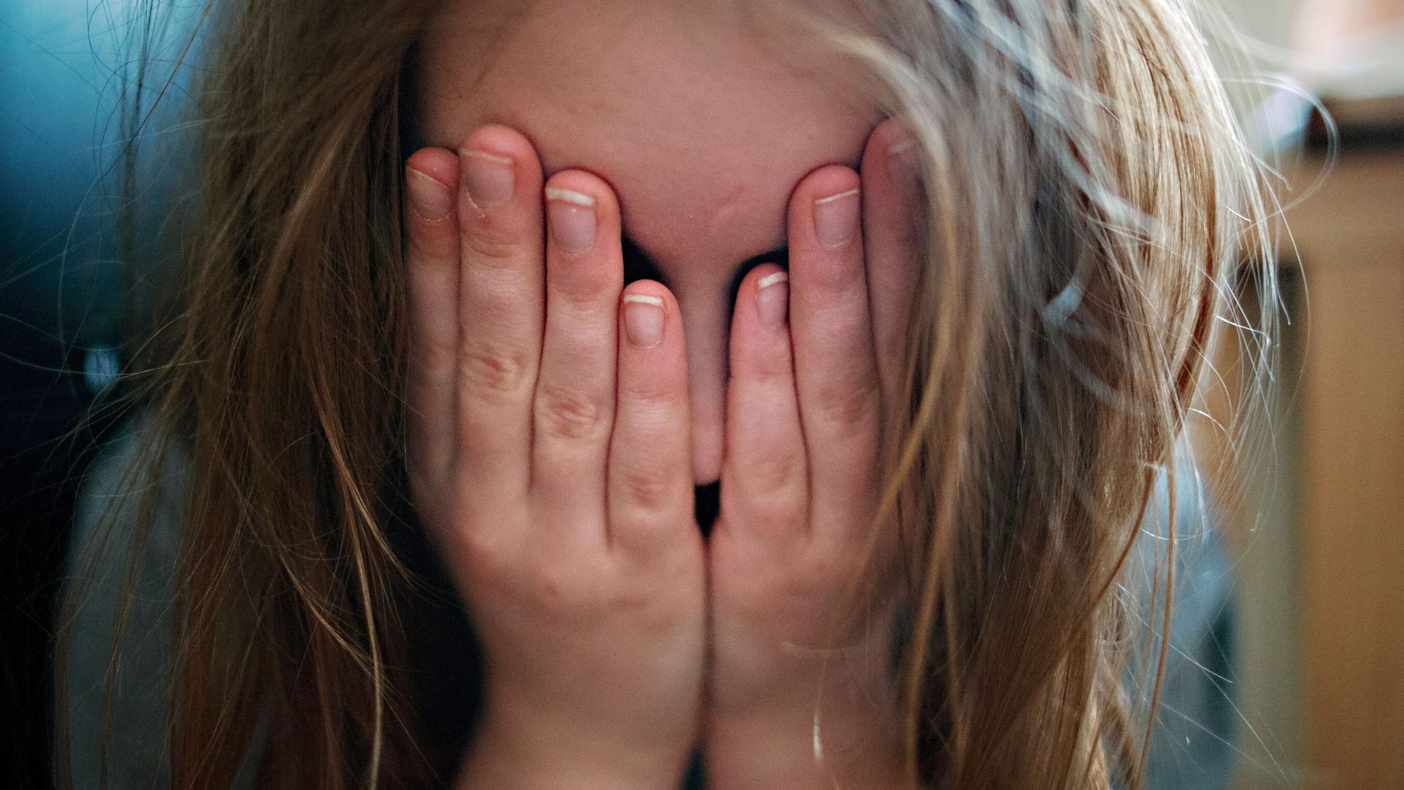Ein junges Mädchen hält sich die Hände vor ihr Gesicht.