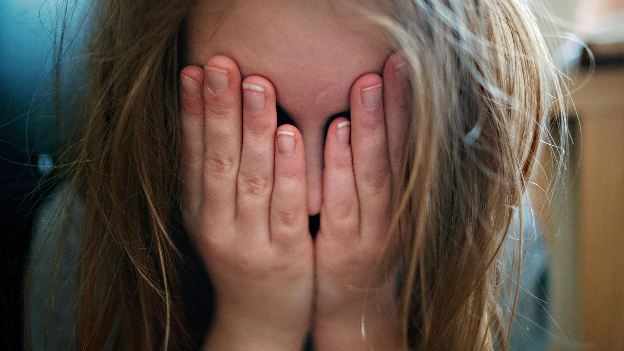 Ein junges Mädchen hält sich die Hände vor ihr Gesicht.